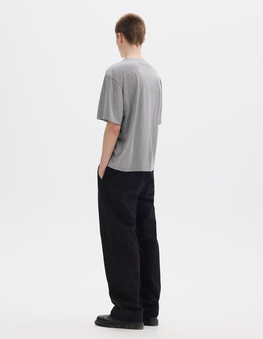 Full body image, back view of model wearing grey relaxed cotton t-shirt with crew neck and boxy cut. Styled with black trousers and black leather shoes.