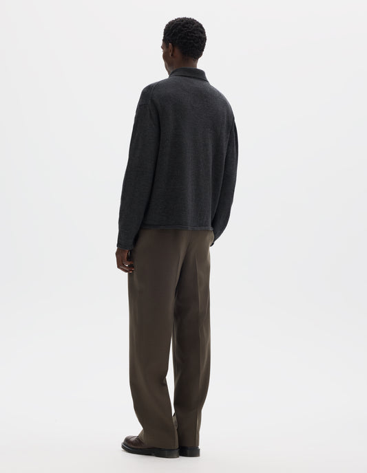 Full body image, back view of model wearing relaxed dark  grey merino cardigan with jersey stitch, fully fashioned collar, set-in fully fashioned sleeves, and tubular hem and cuffs. Styled with brown trousers and brown leather shoes.