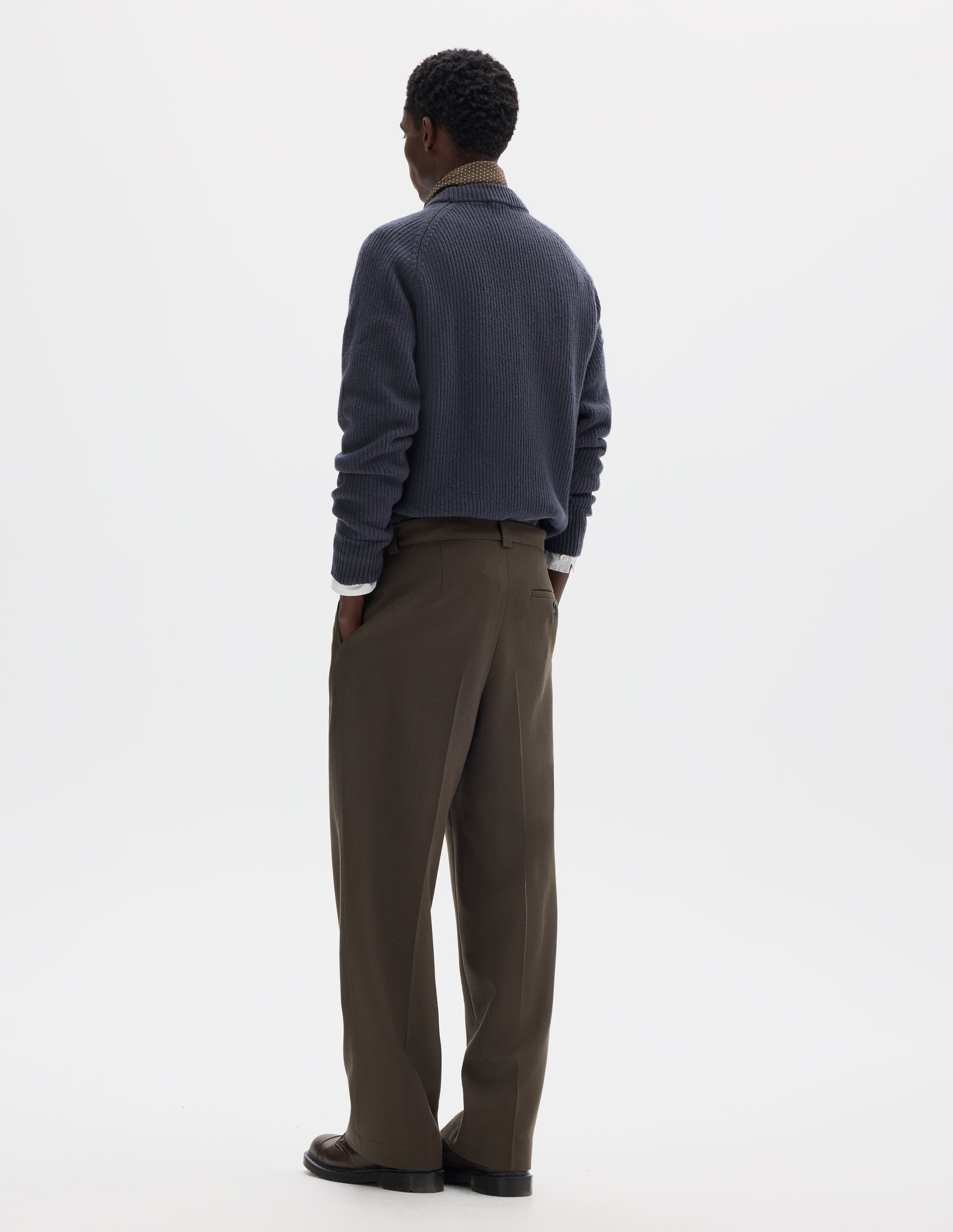 Full body image, back view of model wearing brown straight leg wool trousers with side pockets and horn button-fastening welt back pocket. Styled with grey jumper, white shirt, dark beige silk neck scarf and brown leather shoes.