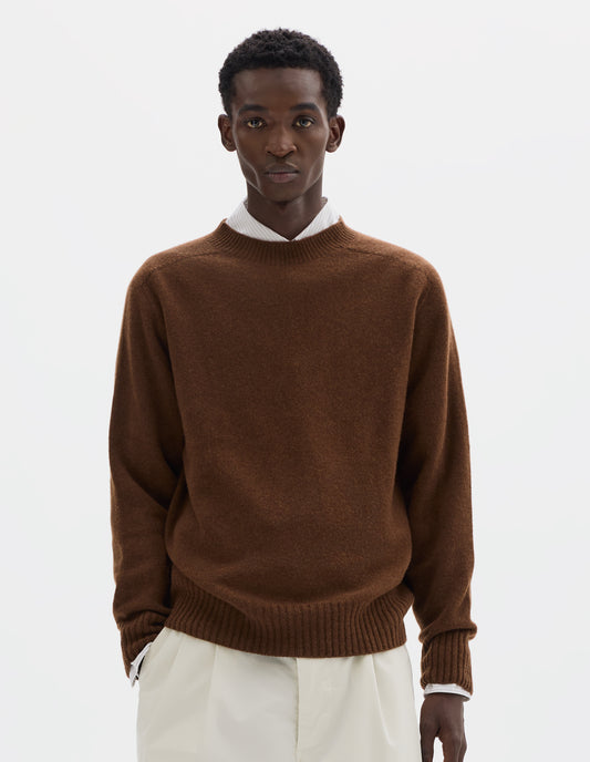 Cropped body image, front view of model wearing brown merino cashmere seamless jumper with ribbed crew neck, cuffs and hem. Styled over white shirt, and with white trousers.