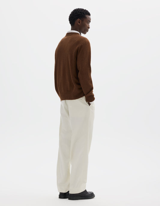 Full body image, back view of model wearing brown merino cashmere seamless jumper with ribbed crew neck, cuffs and hem. Styled over white shirt, and with white trousers and black leather shoes.
