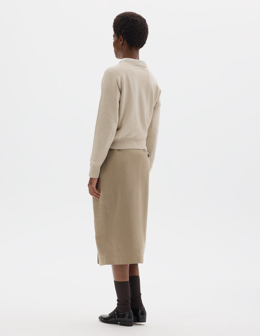 Full body image, back view of model wearing light beige merino cashmere jumper with fully fashioned raglan sleeves with ribbed cuffs and ribbed hem. Styled with beige skirt, dark brown socks and black leather shoes.