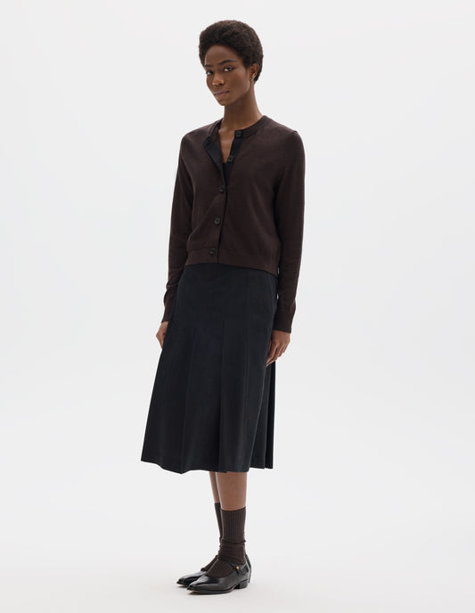 Full body image, front view of model wearing dark brown merino cardigan with fully fashioned sleeves, horn buttons on concealed placket finished with grosgrain, and ribbed neck, cuffs and hem. Styled with black skirt, brown socks and black leather shoes.