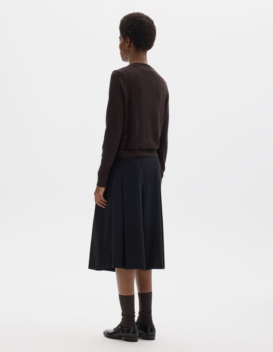 Full body image, back view of model wearing dark brown merino cardigan with fully fashioned sleeves, French shoulder offset on back seam, and ribbed neck, cuffs and hem. Styled with black skirt, brown socks and black leather shoes.
