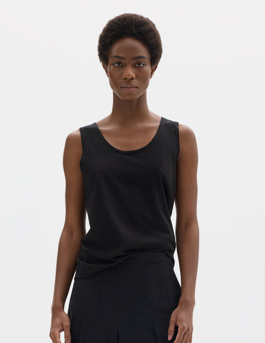 Cropped body image, front view of model wearing black sleeveless cotton vest with scoop neck. Styled with dark grey skirt.