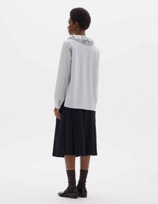 Full body image, back view of model wearing white cotton shirt with dark blue stripes, double ruffle collar, bracelet-length sleeves with mother of pearl buttons on narrow, gathered cuffs, and with curved hem. Styled with dark grey skirt, dark brown socks and black leather shoes.