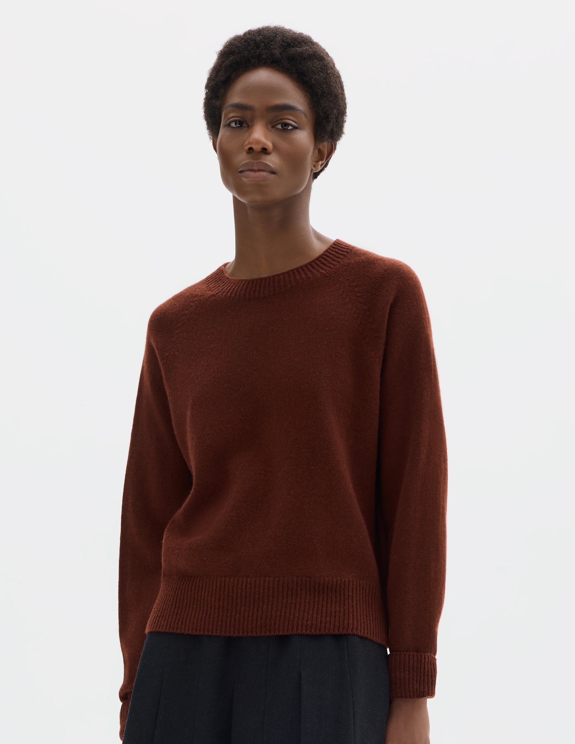 Cropped body image, front view of model wearing brown fully fashioned seamless merino cashmere jumper with crew neck, raglan sleeves, and with ribbed neck, cuffs and hem. Styled with dark grey skirt.