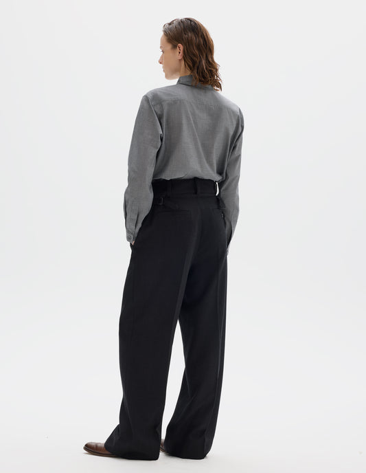 Full body image, back view of model wearing black high waisted wool trousers with dark grey stripes, belt loops on wide waistband, side adjusters and two welt back pockets, one with horn button fastening, and with wide leg. Styled with grey shirt and brown leather brogues.