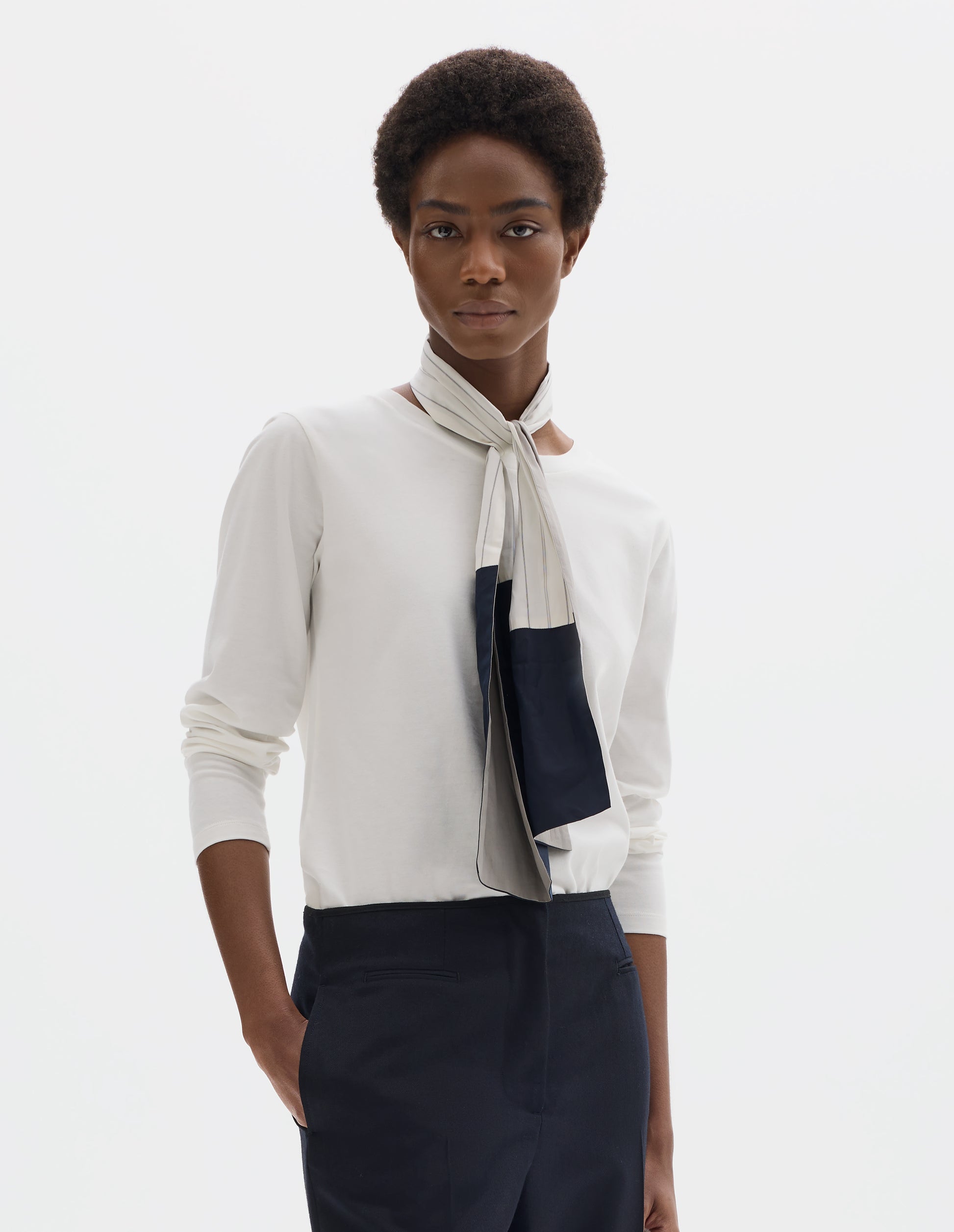 Cropped body image, front view of model wearing white relaxed cotton t-shirt with wide round neck, long sleeves and boxy cut. Styled with white and blue shirting scarf and dark blue trousers.