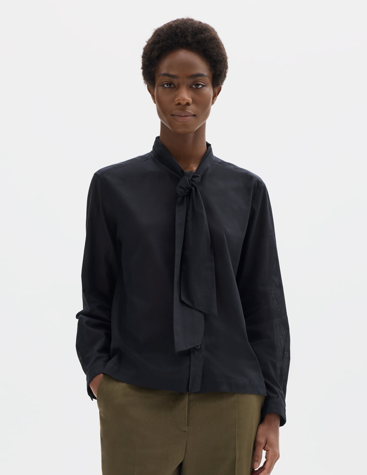 Cropped body image, front view of model wearing black cotton cashmere sheer shirt with attached loose tie, lipped placket, narrow cuffs and with square side split hem. Styled with khaki green trousers.