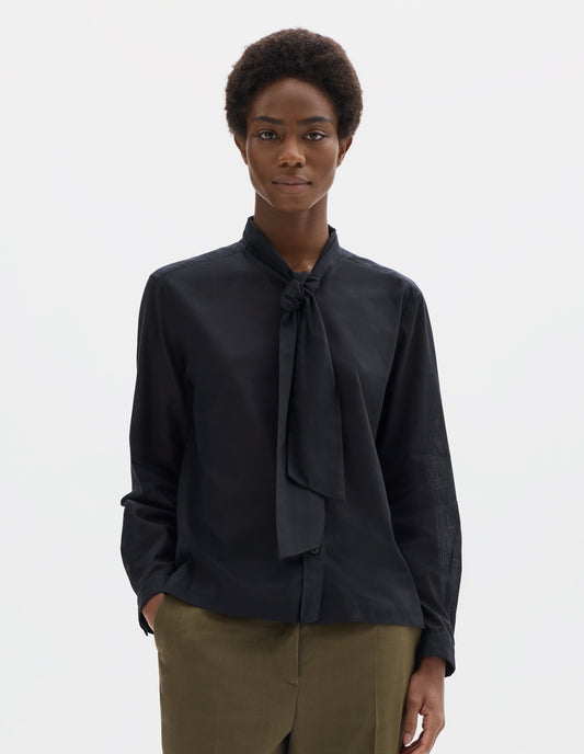 Cropped body image, front view of model wearing black cotton cashmere sheer shirt with attached loose tie, lipped placket, narrow cuffs and with square side split hem. Styled with khaki green trousers.