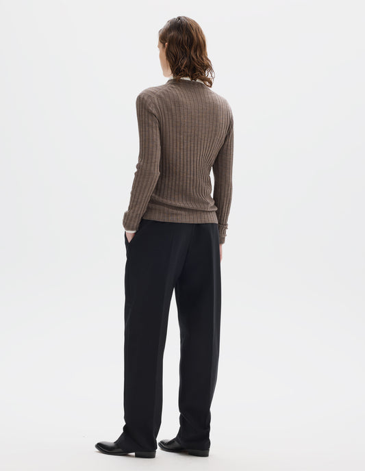 Full body image, back view of model wearing neat fitting dark beige merino top with wide rib through body, wide contrast rib on crew neck, and set-in long sleeves with fine rib cuffs. Styled over white shirt, and with black trousers and black leather shoes.