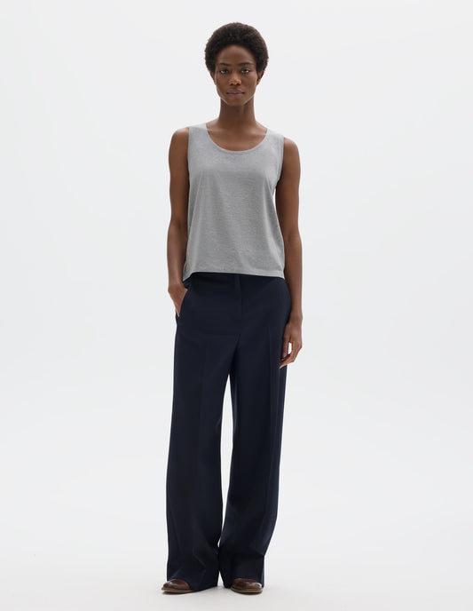 Full body image, front view of model wearing grey sleeveless cotton vest with scoop neck. Styled with dark blue trousers and brown leather brogues.