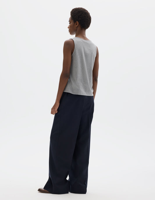Full body image, back view of model wearing grey sleeveless cotton vest. Styled with dark blue trousers and brown leather brogues.