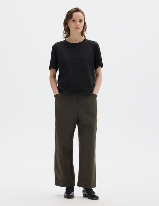 Full body image, front view of model wearing black relaxed cotton t-shirt with crew neck and boxy cut. Styled with brown trousers and black leather shoes.