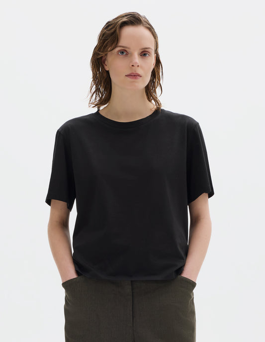 Cropped body image, front view of model wearing black relaxed cotton jersey t-shirt with crew neck and boxy cut. Styled with brown trousers.