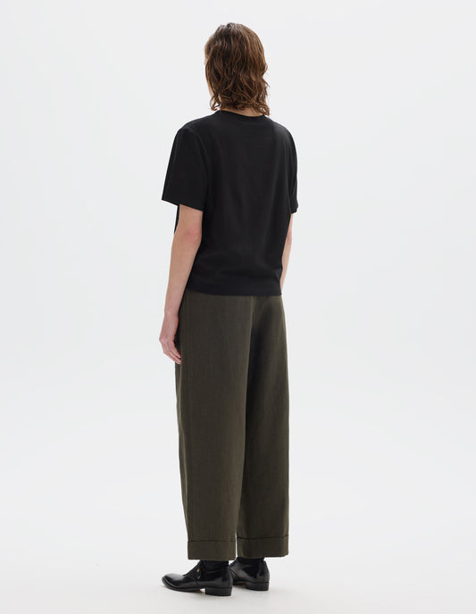 Full body image, back view of model wearing black relaxed cotton t-shirt with crew neck and boxy cut. Styled with brown trousers and black leather shoes.