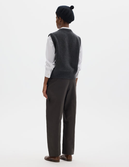 Full body image, back view of model wearing relaxed dark grey cashmere merino knitted gilet with rib detailing at neck, armholes and hem. Styled over white shirt, and with black beret, grey trousers and brown leather brogues. 