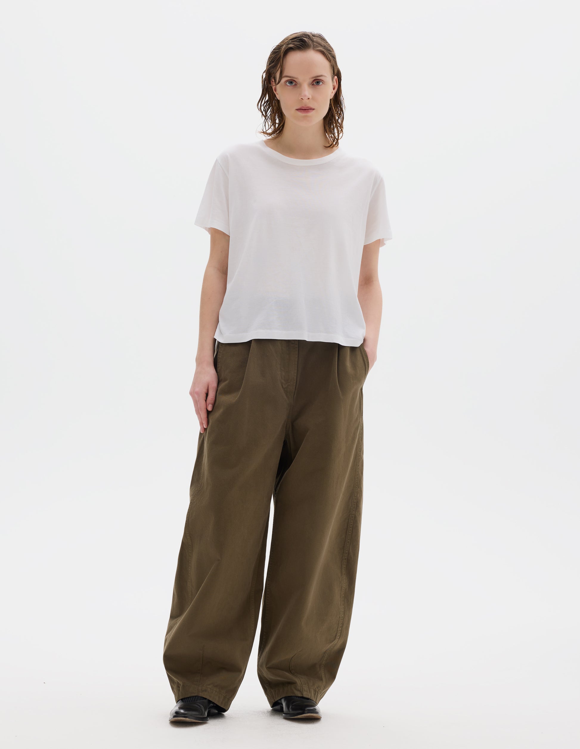 Full body image, front view of model wearing white relaxed cotton t-shirt with crew neck and boxy cut. Styled with khaki green trousers and black leather shoes.