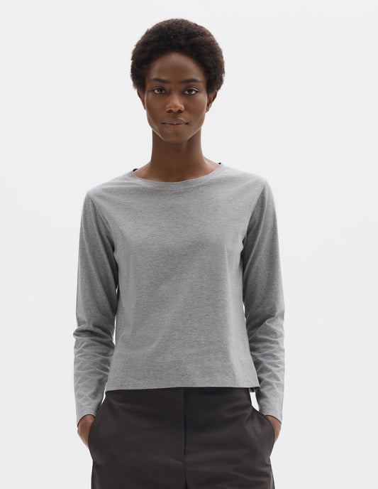 Cropped body image, front view of model wearing grey relaxed cotton t-shirt with wide round neck, long sleeves and boxy cut. Styled with dark grey trousers.