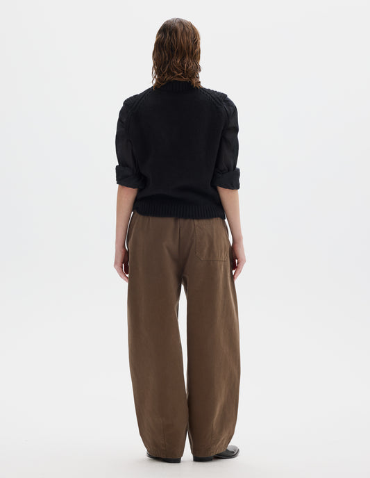 Full body image, back view of model wearing relaxed black wool slipover with plain knitted back and ribbed neck, armholes, side seams and hem. Styled over black black shirt, and with brown trousers and black leather shoes.