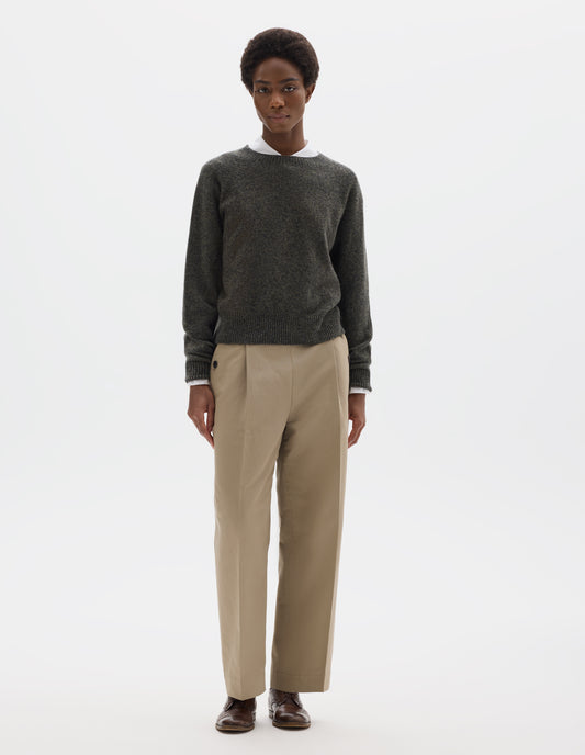 Full body image, front view of model wearing brownish grey fully fashioned seamless merino cashmere  jumper with crew neck, raglan sleeves, and with ribbed neck, cuffs and hem. Styled over white shirt, and with beige trousers and brown leather brogues.