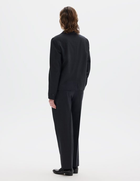 Full body image, back view of model wearing dark grey wool blazer with centre back vent and horn buttons on cuffs. Styled with matching trousers and black leather shoes.