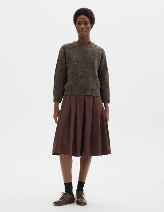 Full body image, front view of model wearing waist length brown crew neck wool jumper with fully fashioned bracelet length raglan sleeves, circular knitted body and wide rib detailing at neck, cuffs and hem. Styled over brown dress, and with black socks and brown leather brogues.
