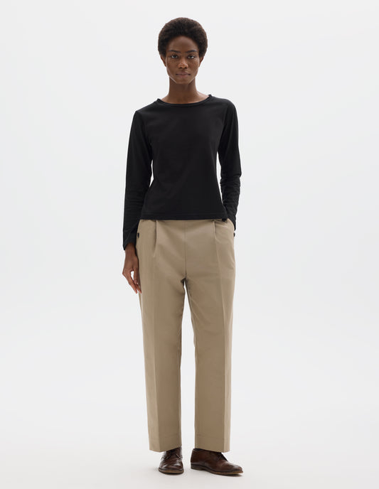 Full body image, front view of model wearing black relaxed cotton t-shirt with wide round neck, long sleeves and boxy cut. Styled with beige trousers and brown leather brogues.