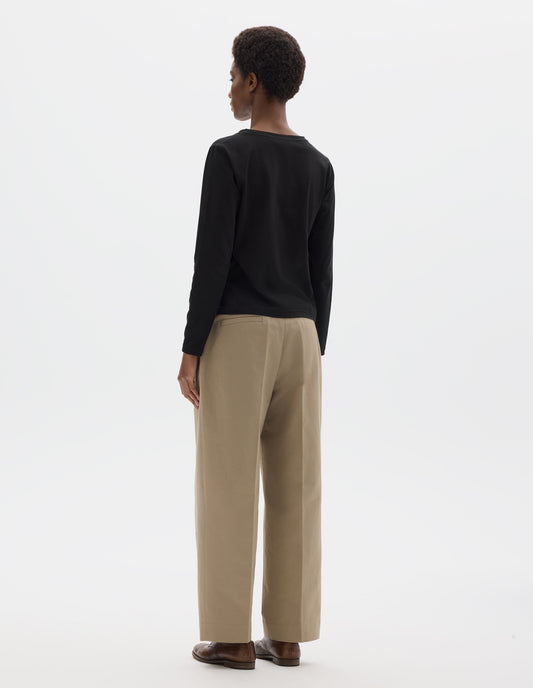 Full body image, back view of model wearing black relaxed cotton t-shirt with wide round neck, long sleeves and boxy cut. Styled with beige trousers and brown leather brogues.