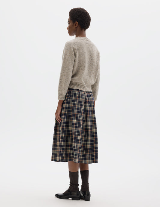 Full body image, back view of model wearing waist length light grey crew neck wool jumper with fully fashioned cropped length raglan sleeves, circular knitted body and wide rib detailing at neck, cuffs and hem. Styled with dark blue and beige checked skirt, brown socks and black leather shoes.