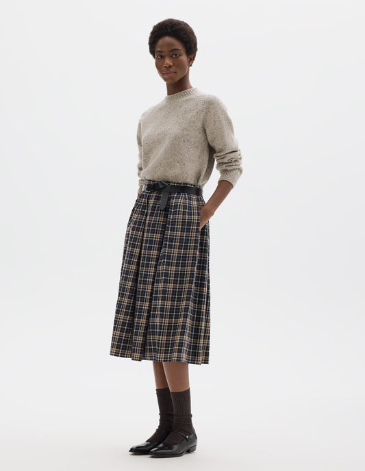 Full body image, front view of model wearing waist length light grey crew neck wool jumper with fully fashioned bracelet length raglan sleeves, circular knitted body and wide rib detailing at neck, cuffs and hem. Styled with dark blue and beige checked skirt, black leather belt, brown socks and black leather shoes.
