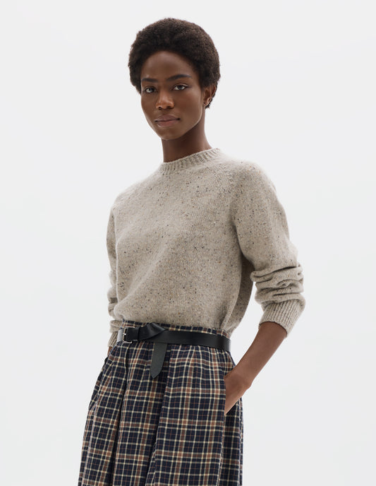 Cropped body image, front view of model wearing waist length light grey crew neck wool jumper with fully fashioned bracelet length raglan sleeves, circular knitted body and wide rib detailing at neck, cuffs and hem. Styled with dark blue and beige checked skirt and black leather belt.