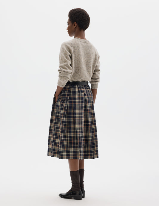 Full body image, back view of model wearing waist length light grey crew neck wool jumper with fully fashioned bracelet length raglan sleeves, circular knitted body and wide rib detailing at neck, cuffs and hem. Styled with dark blue and beige checked skirt, black leather belt, brown socks and black leather shoes.