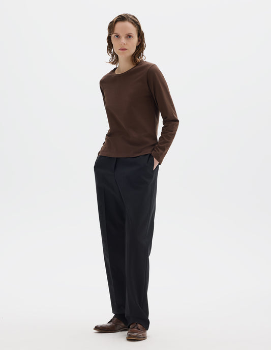 Full body image, front view of model wearing relaxed dark brown jersey t-shirt with boxy cut, wide neck and long sleeves. Styled with black trousers and brown leather brogues.