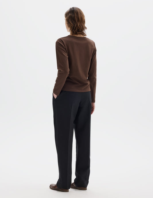 Full body image, back view of model wearing relaxed dark brown jersey t-shirt with boxy cut, wide neck and long sleeves. Styled with black trousers and brown leather brogues.