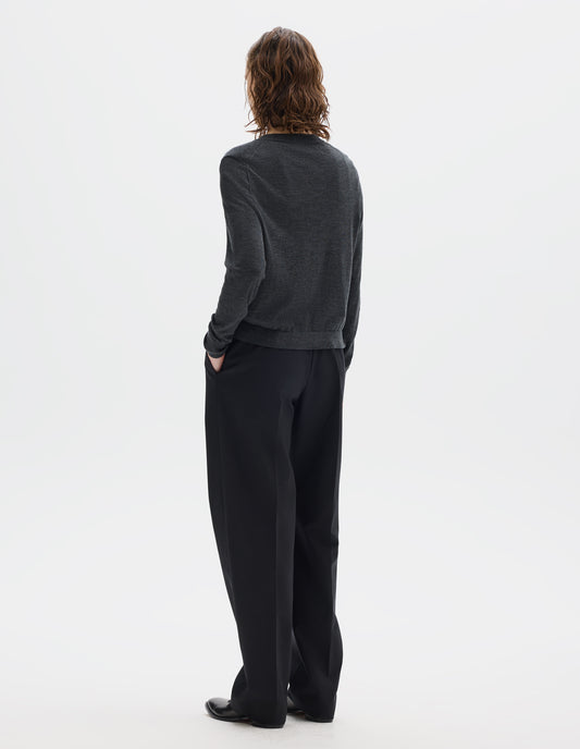 Full body image, back view of model wearing dark grey merino cardigan with fully fashioned sleeves, French shoulder offset on back seam, and ribbed neck, cuffs and hem. Styled with black trousers and black leather shoes.