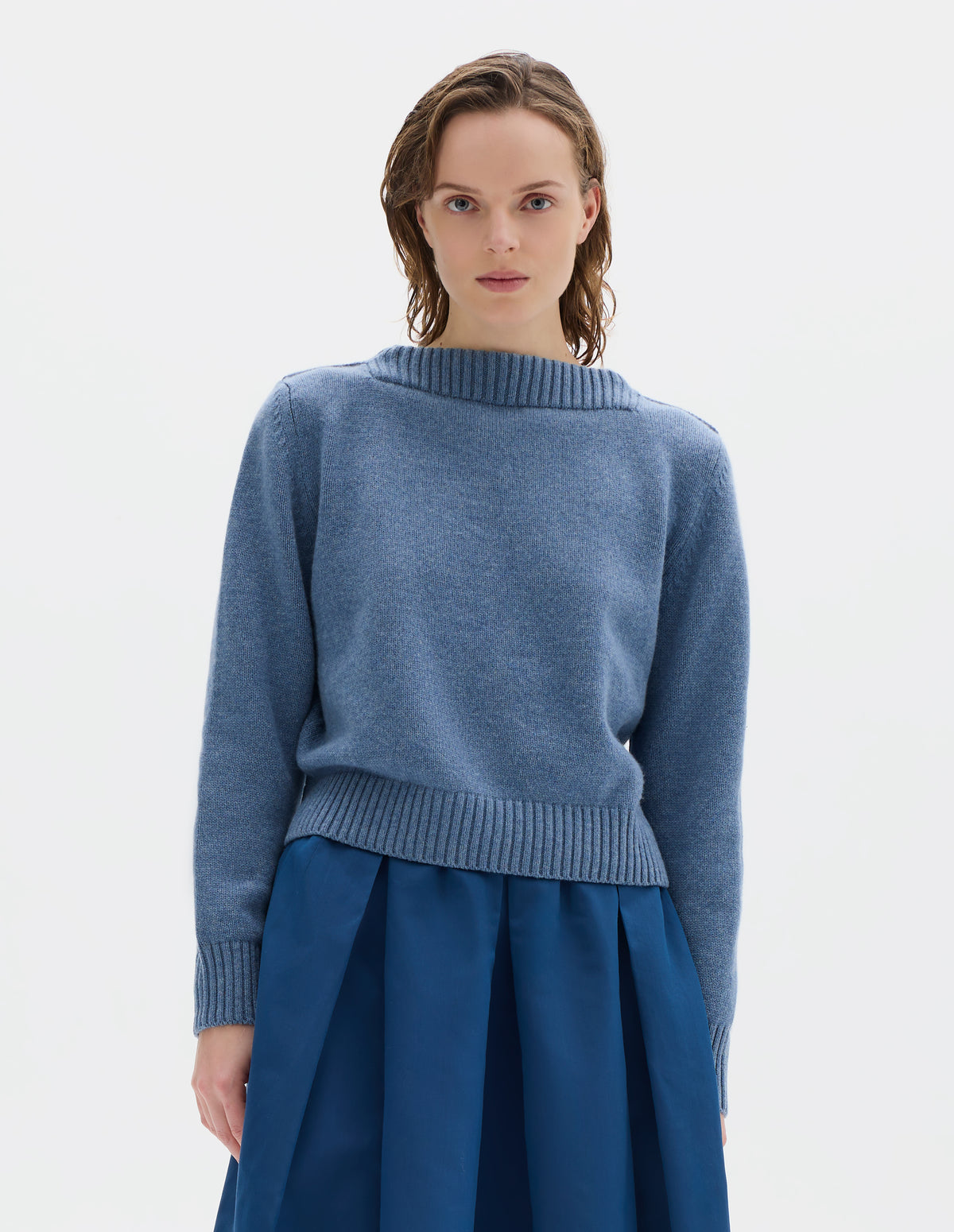 Cropped body image, front view of model wearing cropped light blue merino cashmere fully fashioned jumper with higher square neckline and with wide rib detailing on neck, cuffs and hem. Styled with blue skirt.