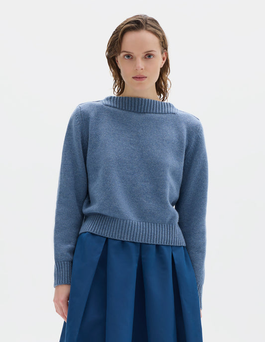 Cropped body image, front view of model wearing cropped light blue merino cashmere fully fashioned jumper with higher square neckline and with wide rib detailing on neck, cuffs and hem. Styled with blue skirt.