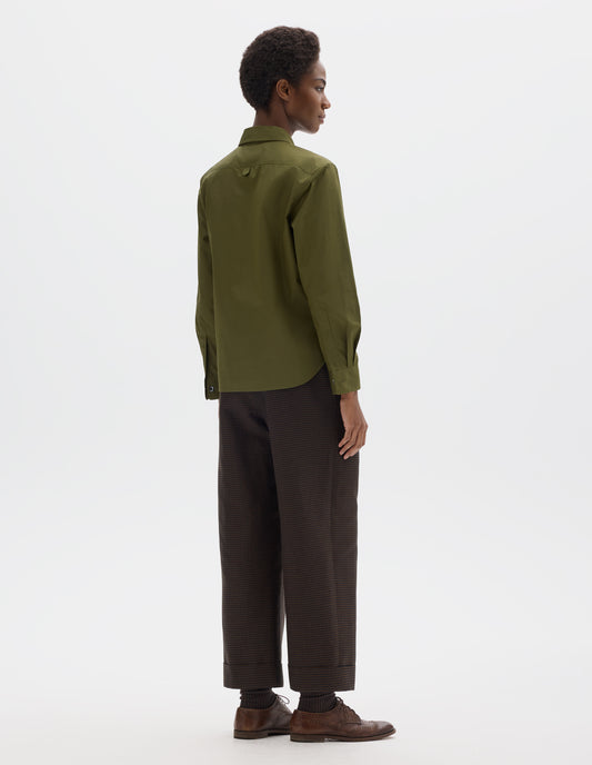 Full body image, back view of model wearing green cotton shirt with hanger loop detail on back yoke, mother of pearl buttons on cuffs and curved hem.  Styled with brown trousers and brown leather brogues.
