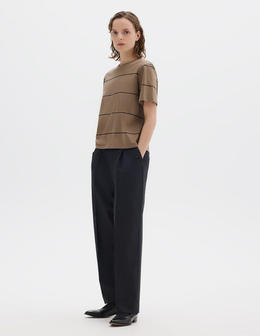 Full body image, front view of model wearing  relaxed beige jersey t-shirt with black stripes, boxy cut and with crew neck. Styled with dark grey trousers and black leather shoes.