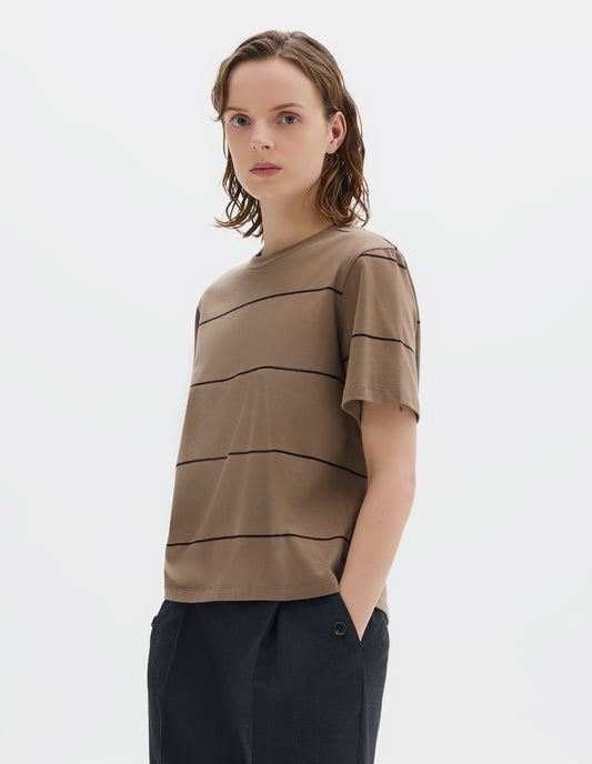 Cropped body image, front view of model wearing relaxed beige jersey t-shirt with black stripes, boxy cut and with crew neck. Styled with dark grey trousers.