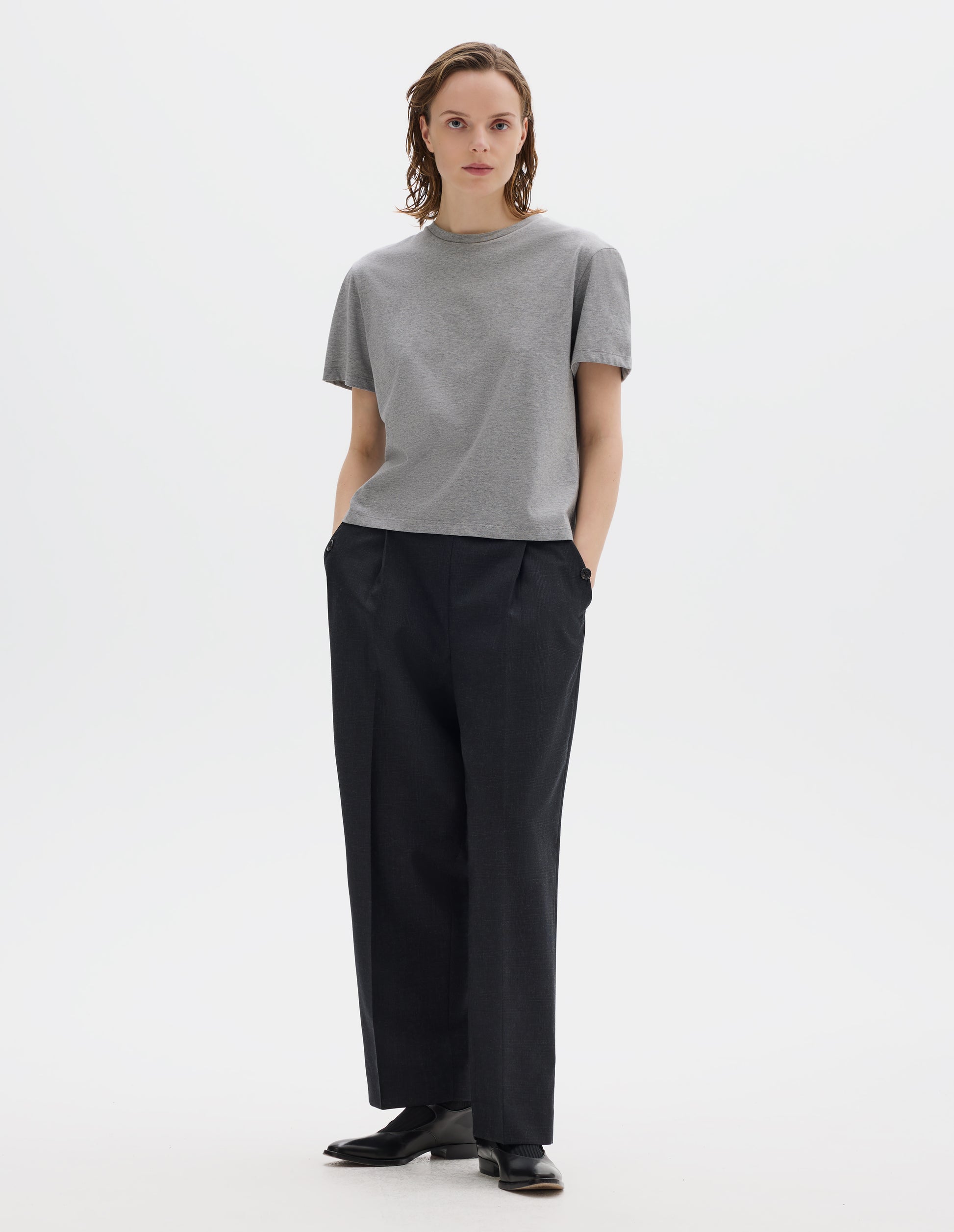 Full body image, front view of model wearing grey relaxed cotton t-shirt with crew neck and boxy cut. Styled with dark grey trousers and black leather shoes.