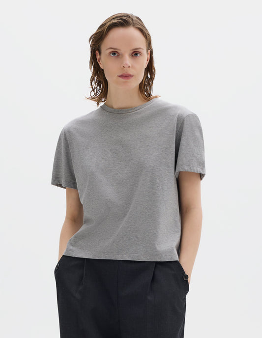Cropped body image, front view of model wearing grey relaxed cotton jersey t-shirt with crew neck and boxy cut. Styled with dark grey trousers.