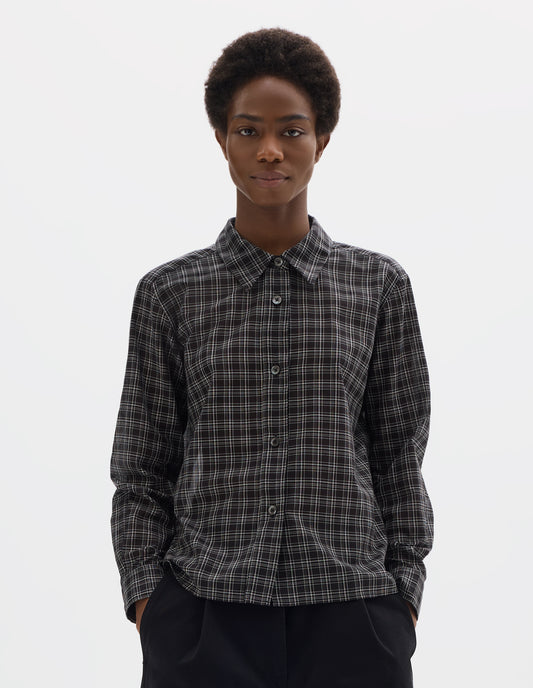 Cropped body image, front view of model wearing black and white cotton check shirt with mother of pearl buttons on placket, stepped hem with curved front and straight-cut back. Styled with black trousers.
