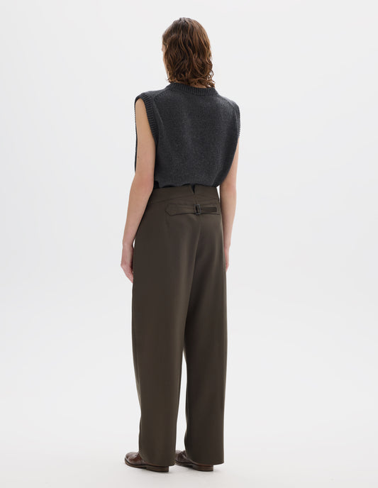 Full body image, back view of model wearing high waisted brown wool trousers with back cinch. Styled with grey knitted gilet and brown leather brogues.