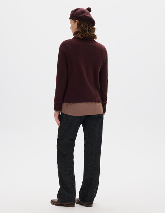 Full body image, back view of model wearing seamless dark red cashmere roll neck jumper with contrast ribbing on neck, cuffs and hem. Styled over light brown shirt, and with dark brown beret, black jeans and brown leather brogues.