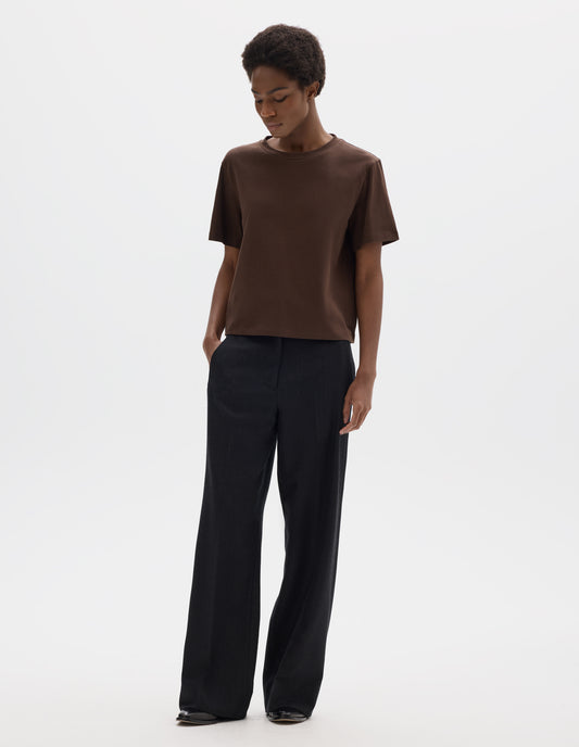 Full body image, front view of model wearing relaxed dark brown jersey t-shirt with crew neck and boxy cut. Styled with dark blue trousers and black leather shoes.