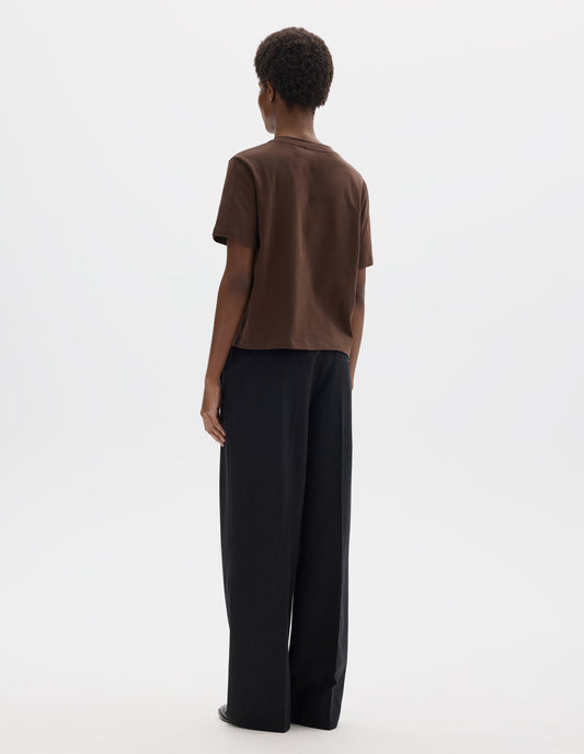 Full body image, back view of model wearing relaxed dark brown jersey t-shirt with crew neck and boxy cut. Styled with dark blue trousers and black leather shoes.