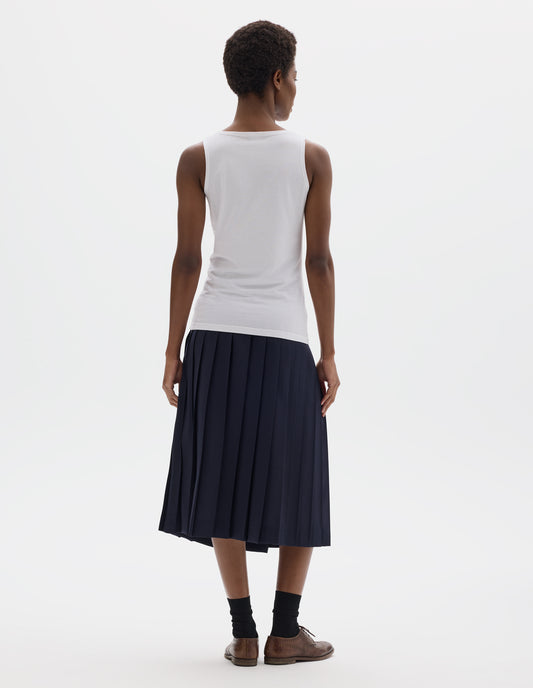 Full body image, back view of model wearing white sleeveless cotton vest. Styled with dark blue skirt, black socks and dark brown leather brogues.